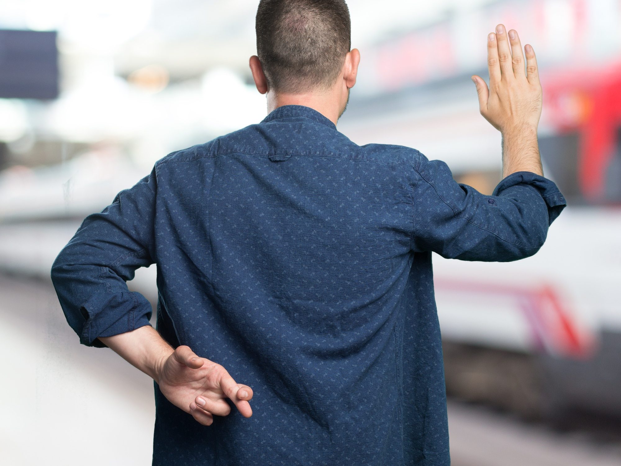 Mann steht mit dem Rücken zur Kamera und eine Hand auf dem Rücken, die Finger sind verschränkt.