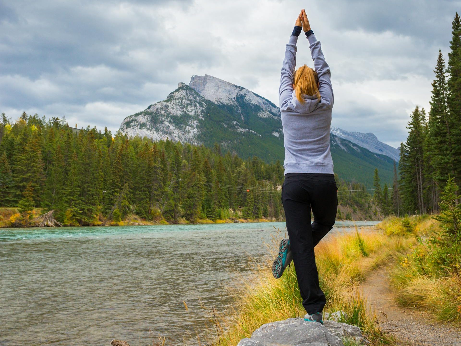 Eine Frau macht in offener Landschaft Yoga stehend.