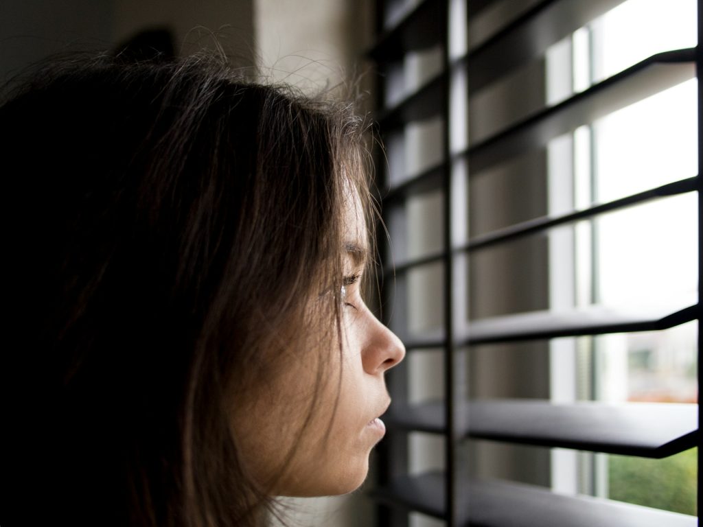 Der Kopf einer Frau im Profil, sie schaut ernst aus einem Fenster raus.