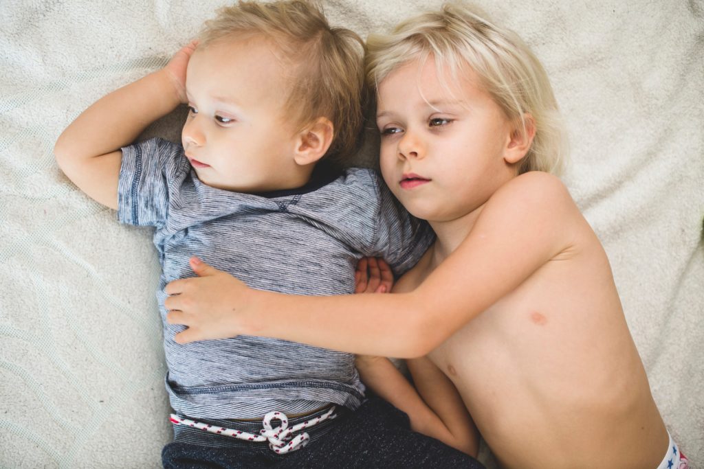 Zwei junge Geschwisterkinder liegen entspannt im Bett.