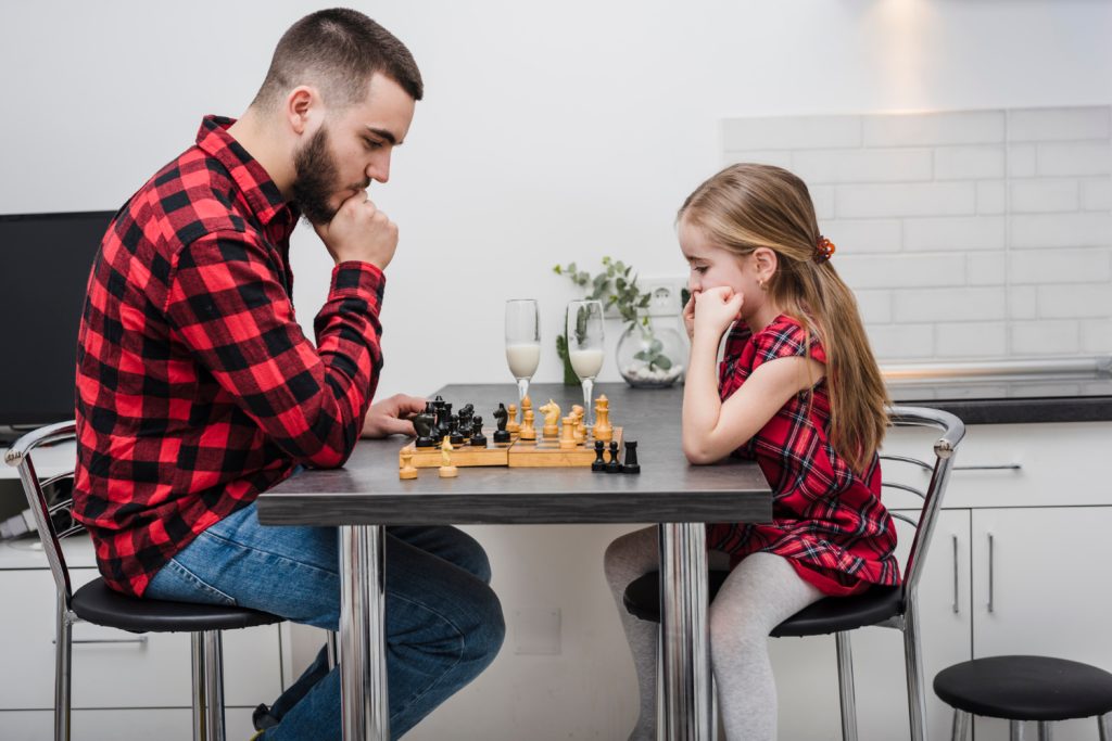 Vater und Tochter sitzen sich gegenüber und Spielen Schach.