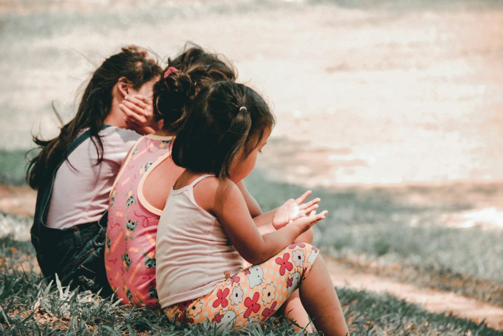 Drei Kinder in Rückenansicht sitzen nebeneinander und erzählen.