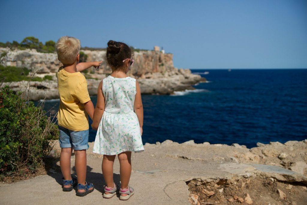 Zwei Kinder stehen am Meeresufer und schauen aufs Meer hinaus