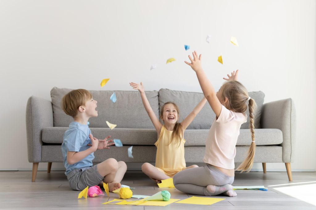 Drei Kinder sitzen im Kreis und werfen Konfetti in die Luft.